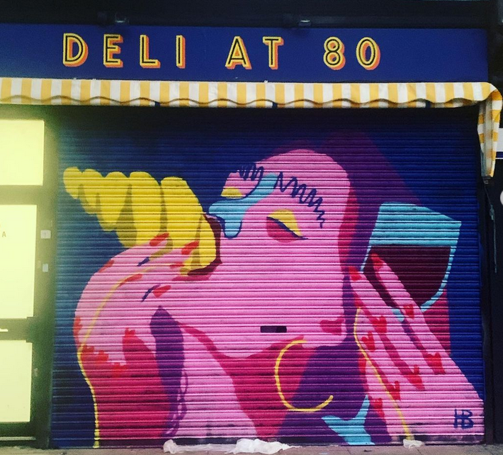 A mural of a woman holding a glass of red wine and eating a croissant on the shutter of Deli at 80 shop in Finsbury Park, North London.